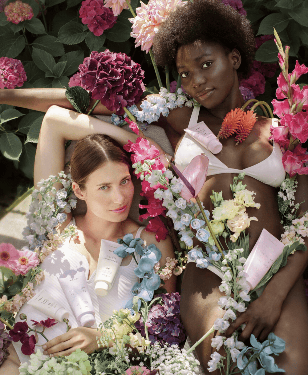 Zwei Personen umgeben von Blumen mit Sonnencreme von V.SUN
